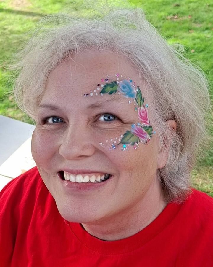 Pastel flower face design with leaves and gems on an adult guest