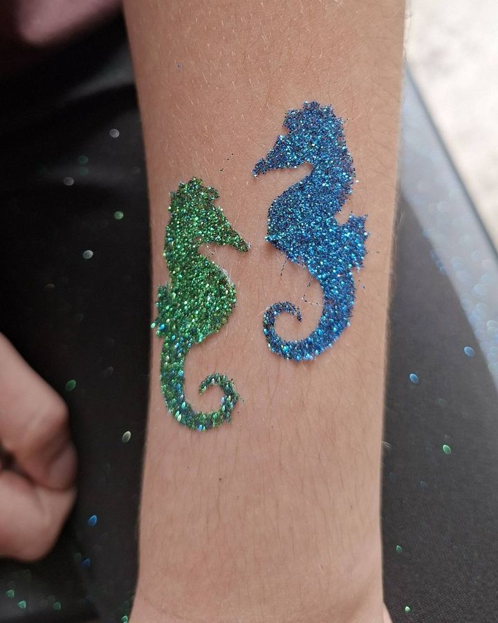 Green and blue seahorse glitter tattoos on an arm